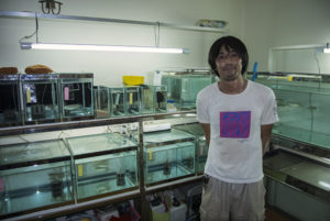 Tomoyuki Sato standing proudly before his home laboratory and fishroom