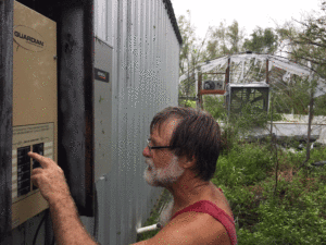 After Hurricane Harvey, Charles Clapsaddle finds himself wiring up new circuits for well, freezers, refrigerator, and chargers, with tattered greenhouse in background.